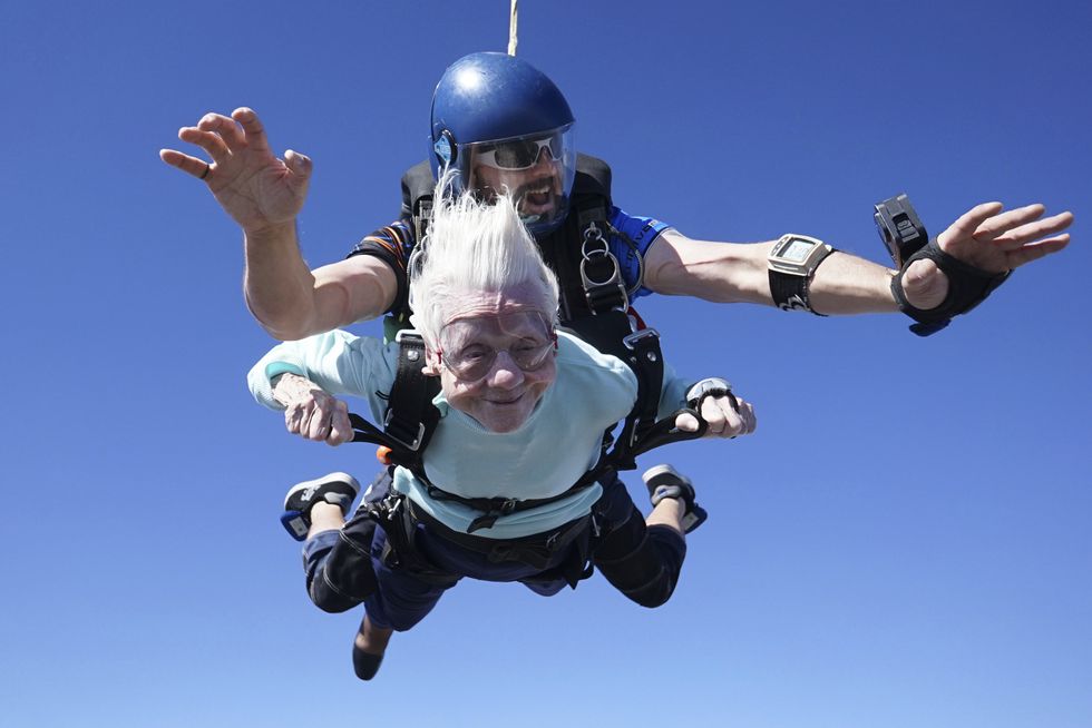 A 104-year-old white woman with white hair and a blue jumper, skydiving.
