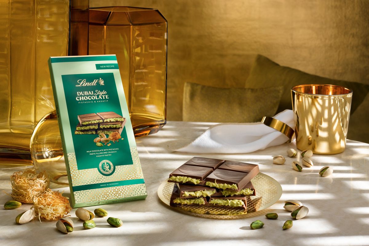 A bar of Lindt's take on Dubai chocolate sits on a table surrounded by pistachio nuts