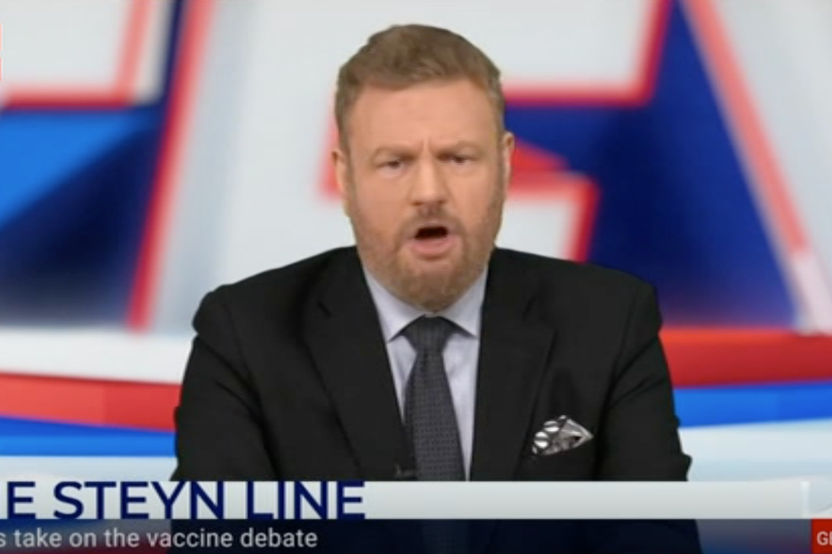 A bearded white man with short brown hair, a beard and a black suit, presenting a TV show.