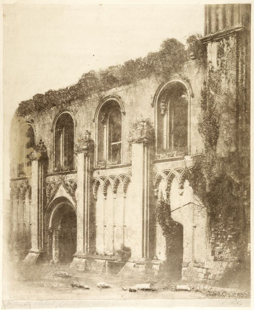 A black and white photograph of the side of a castle covered in ivy