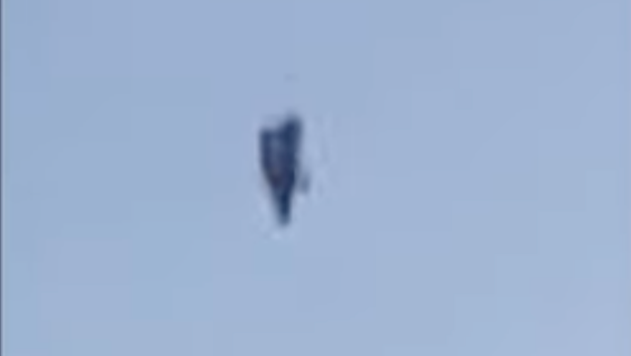 A black, upright object hovering in a blue sky.