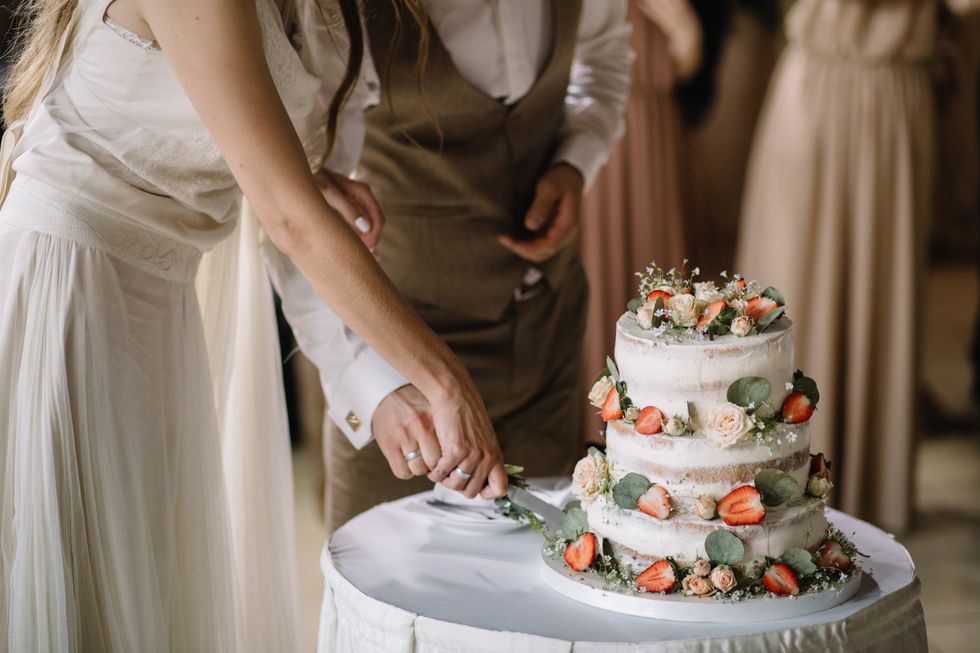 A bride and groom cutting a floral wedding cake on a table.