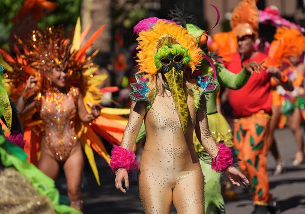 A carnival-goer in a gold leotard and a mask with a long bird's beak