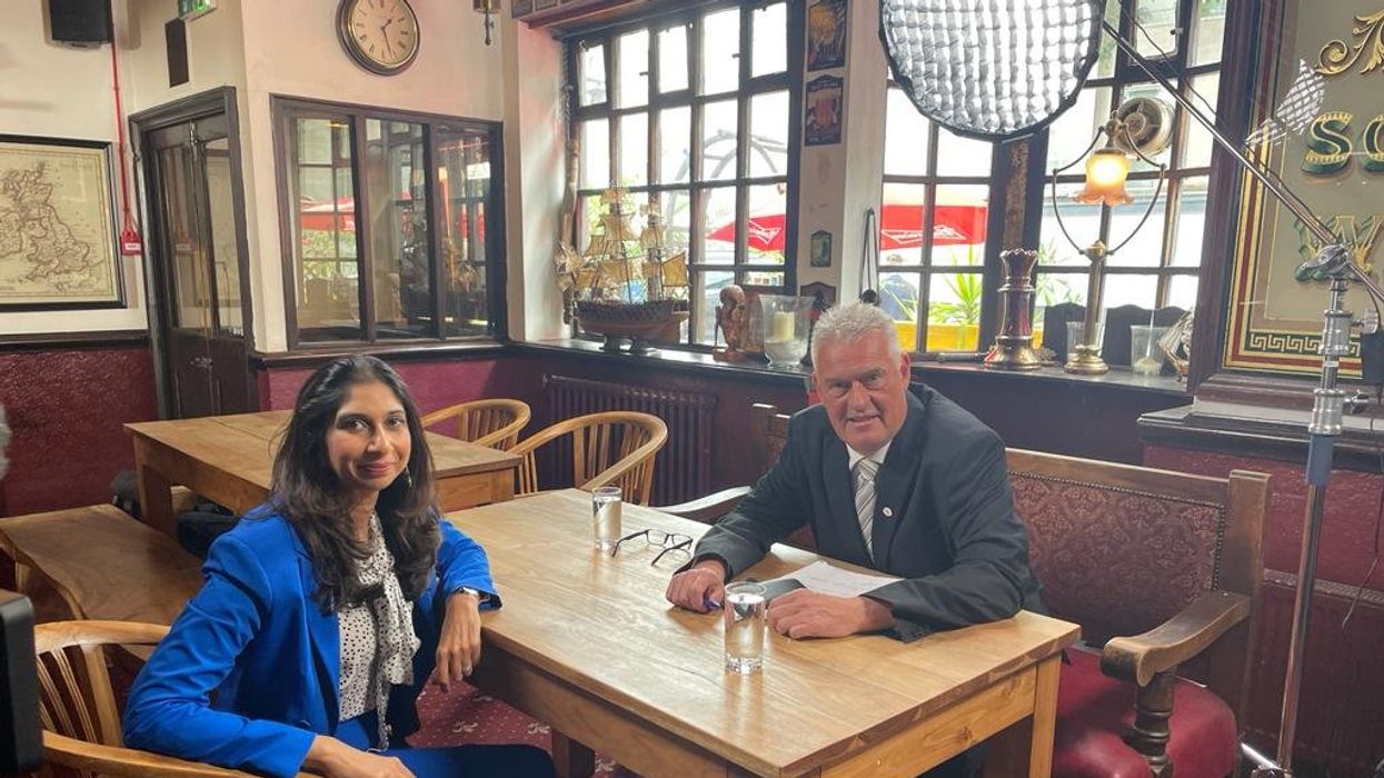 A dark-haired woman sits across a table from a grey-haired man, as they both smile at the camera