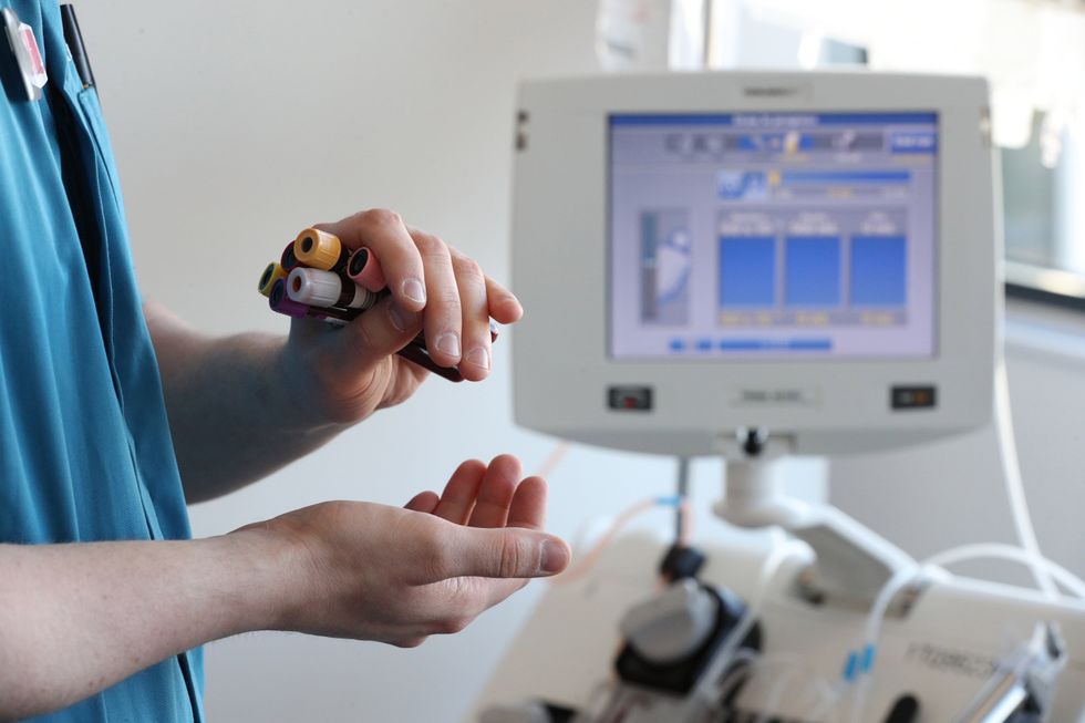A donor carer holds vials of blood in front of an apheresis machine which separates plasma from blood (Jonathan Brady/PA)
