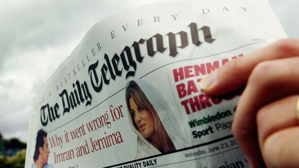 A front page of The Daily Telegraph, with a hand visible on the right holding it up.