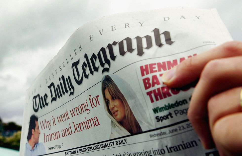 A front page of The Daily Telegraph, with a hand visible on the right holding it up.