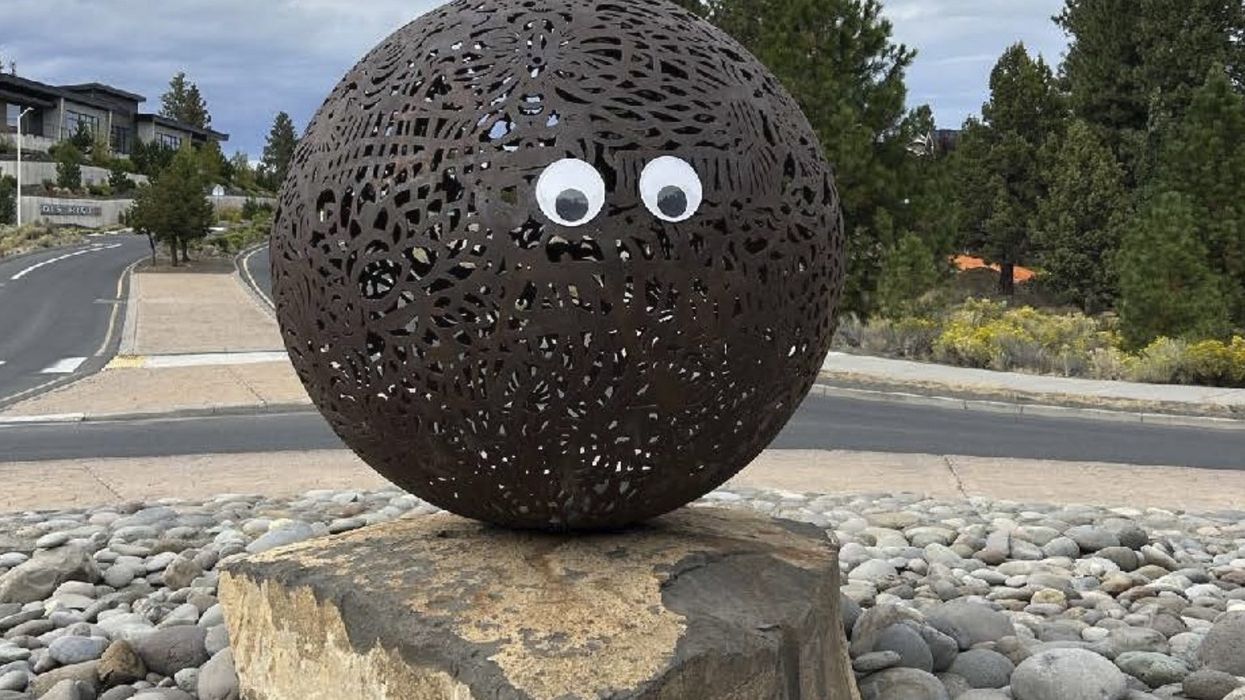 A giant metal ball artwork has two large googly eyes affixed to it.