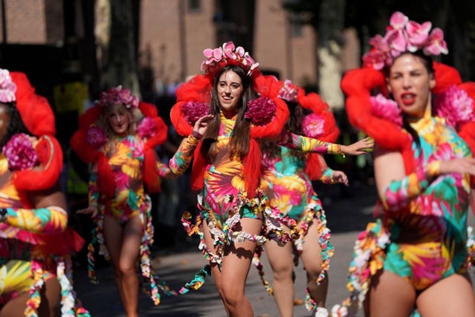 A group of dancers in tropical print with large red collars and flowers on their heads