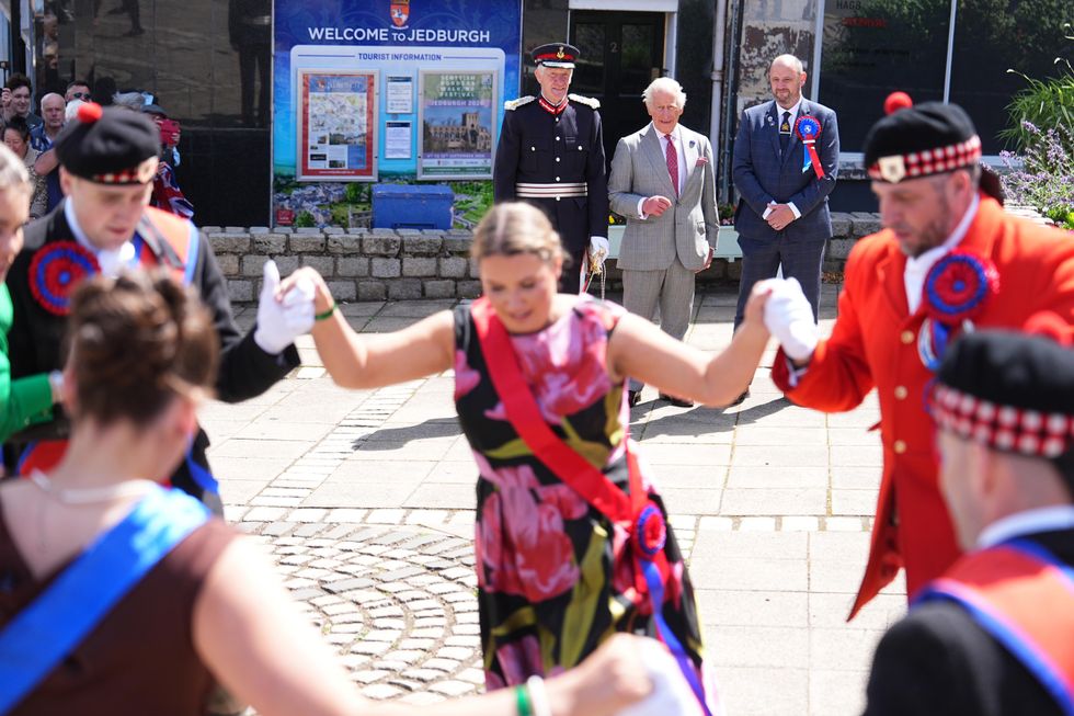 A group of dancers performing on a street while the King watches on in the background