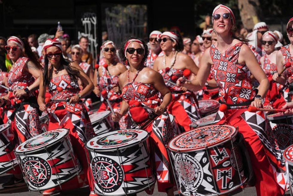 A group of women in red and black tribal patterned cloth banging drums