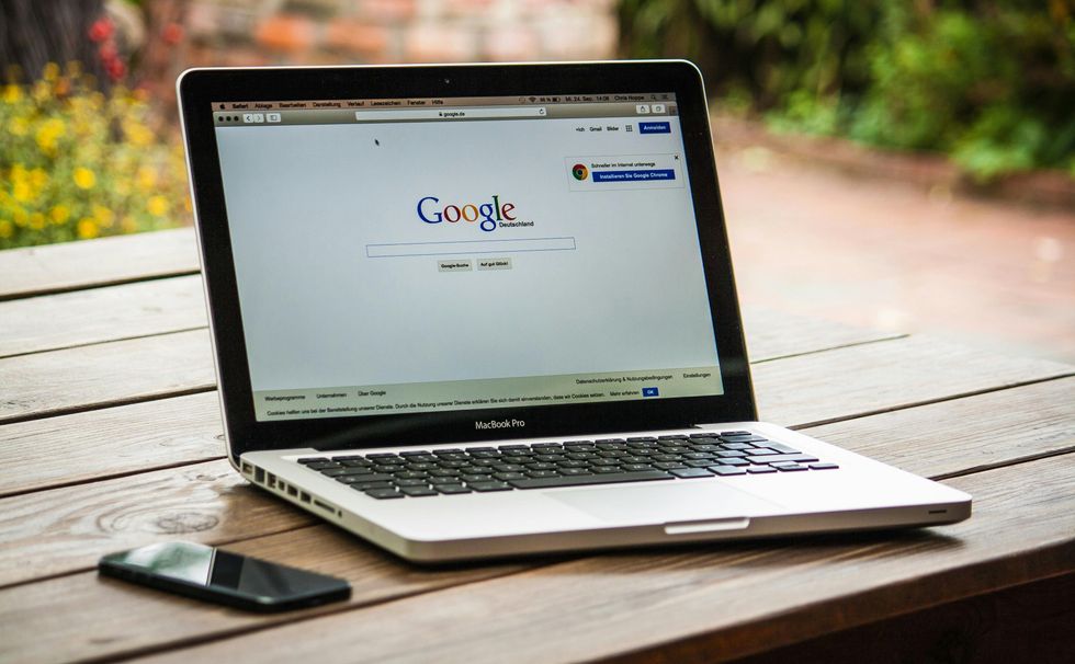 A laptop with Google open sits on a wooden table next to an iPhone