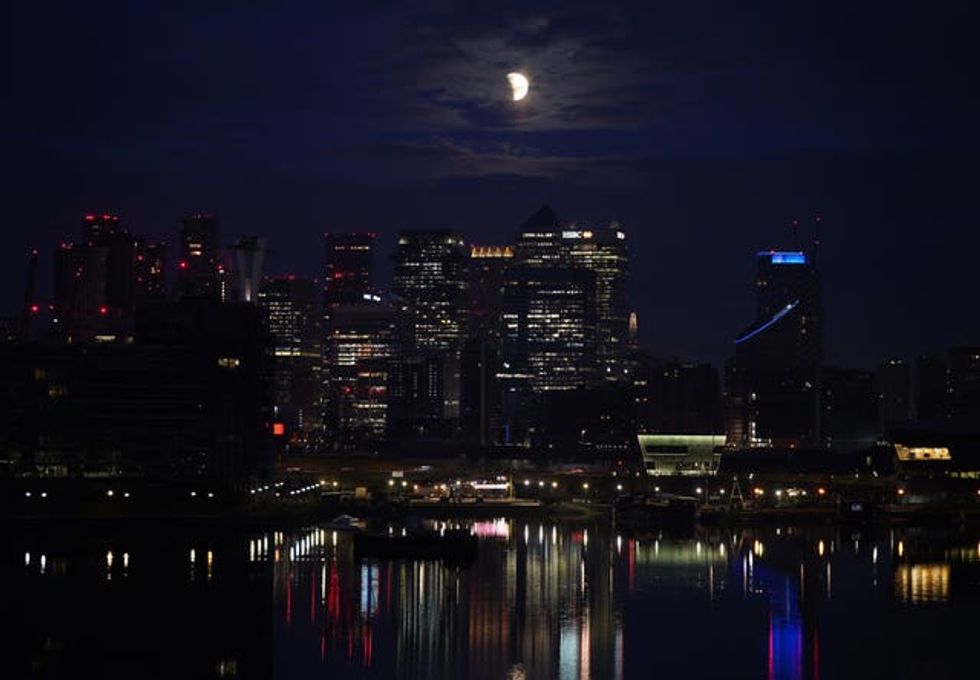 A lunar eclipse is visible above Canary Wharf in London as the full moon passes into Earth\u2019s shadow