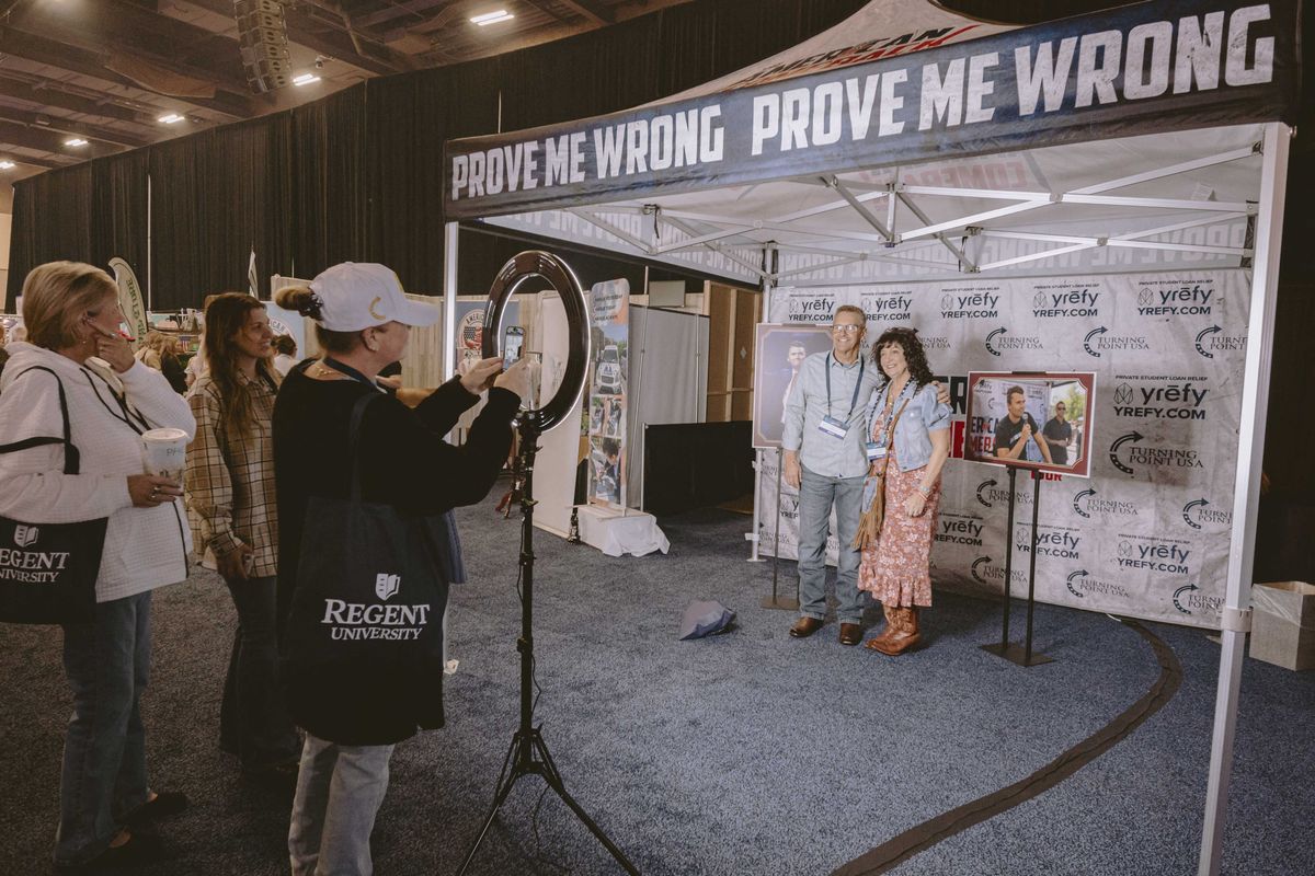 A man and a woman pose for a photo inside a Turning Point USA 'Prove Me Wrong' tent.