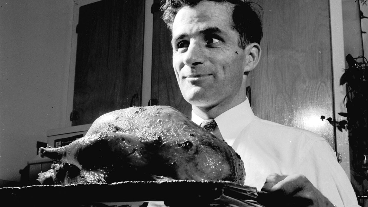 A man bringing a roast turkey to the table for a traditional Christmas dinner, circa 1955