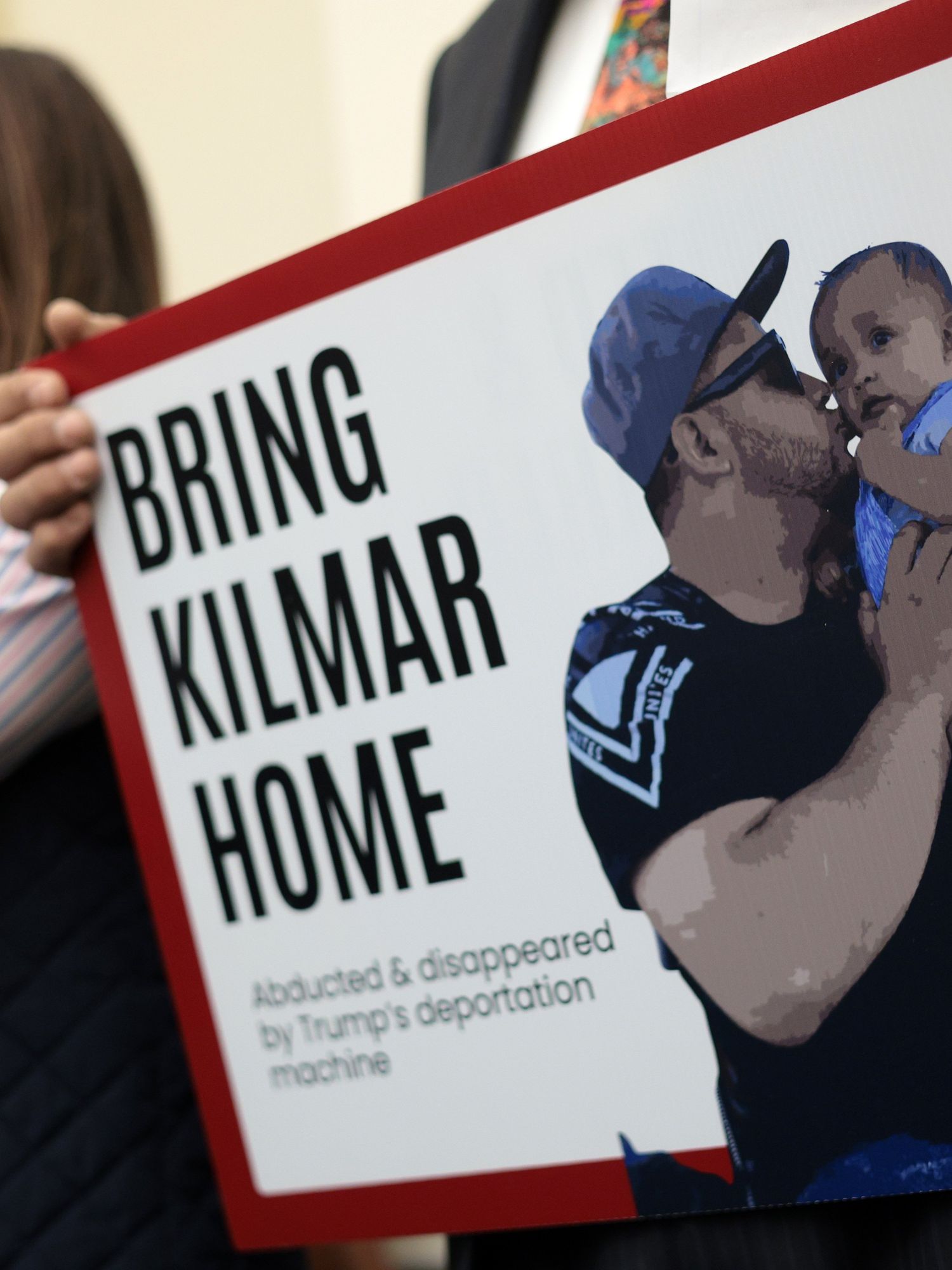 A man holds up a picture of Kilmar Abrego Garcia holding and kissing his child, with the text 'Bring Kilmar home' on it.