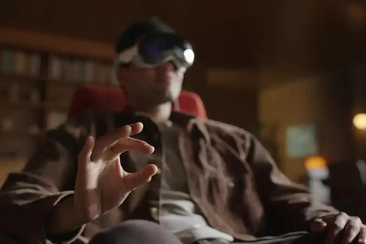 A man in a brown jacket mimics a hand gesture with his index finger and thumb to control his Apple Vision Pro