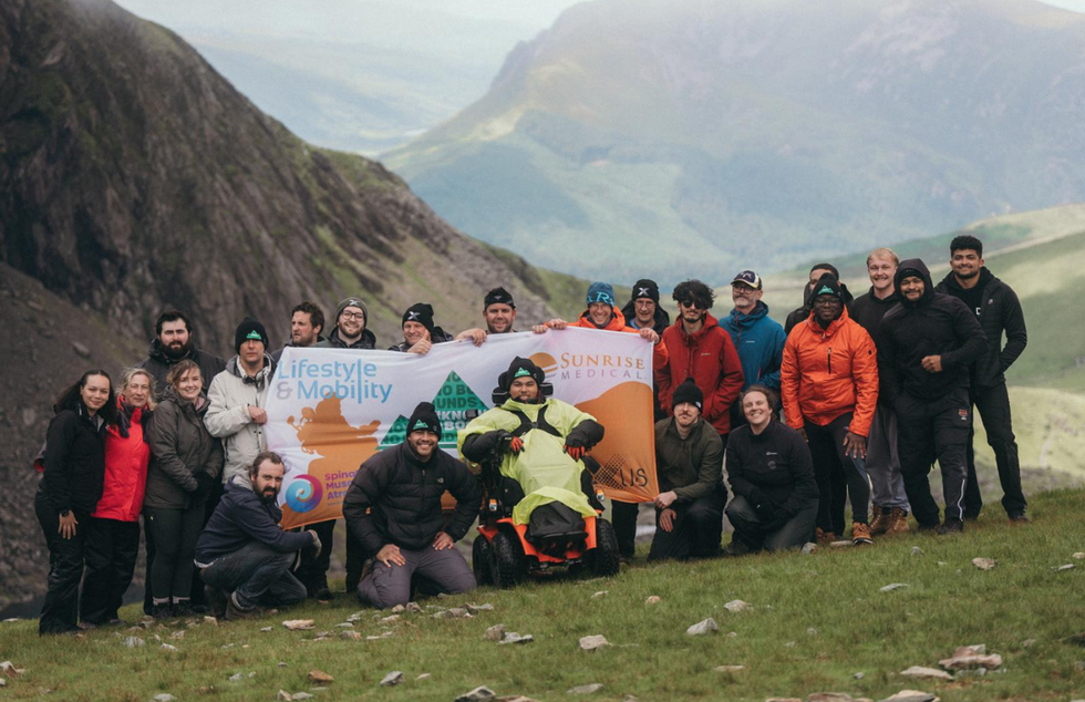 A man in a wheelchair with a group of about 25 people standing on a hillside