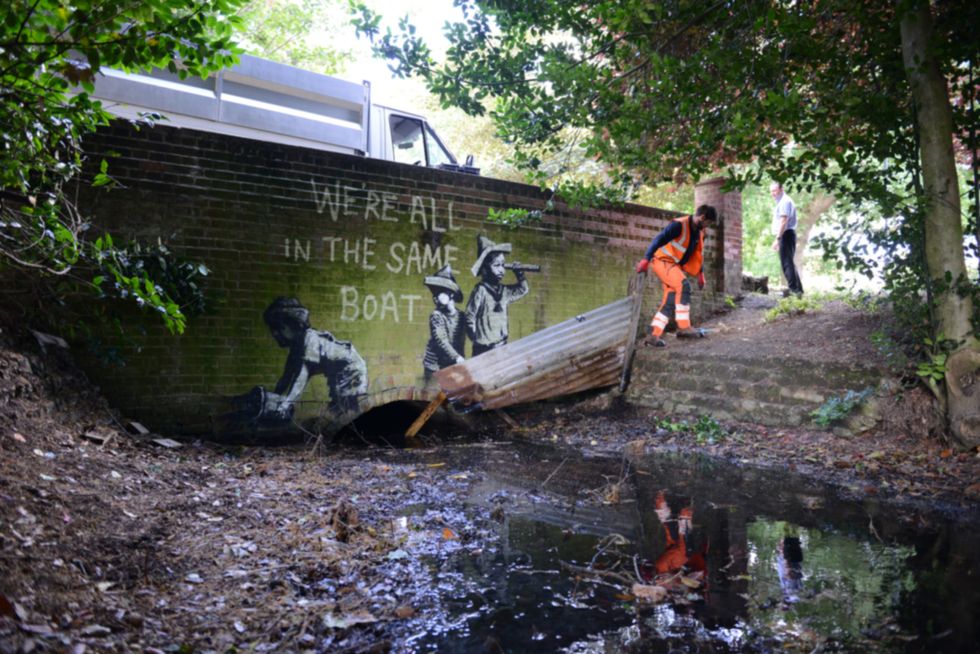 A man in orange overalls removes part of the piece of street art (PA)