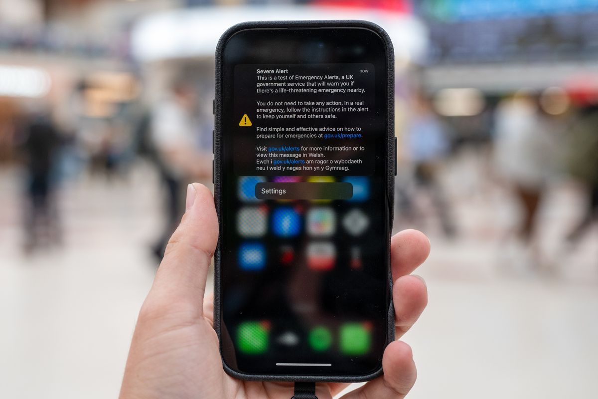 A mobile phone held up in a public space displays the emergency alert on-screen.