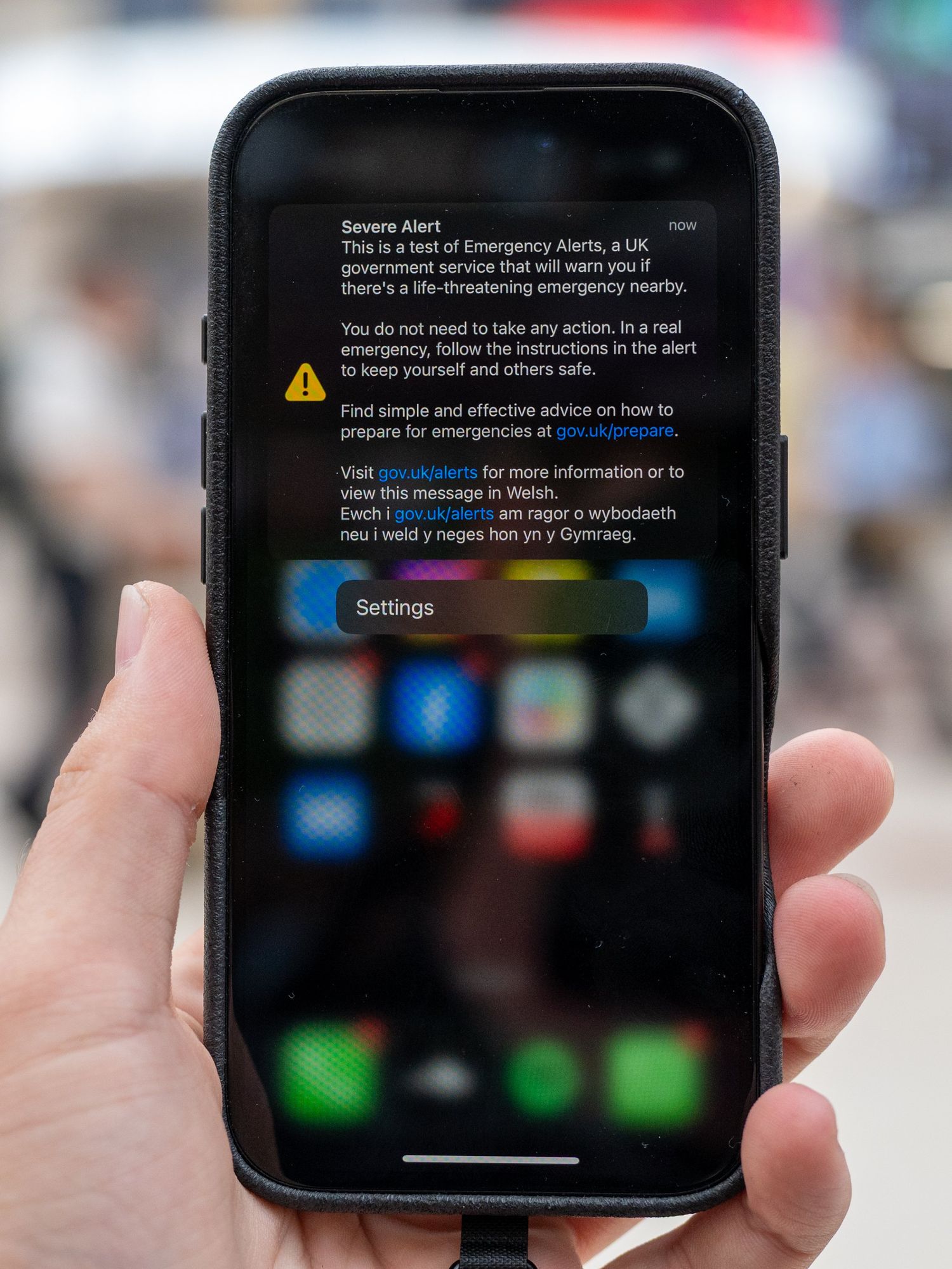 A mobile phone held up in a public space displays the emergency alert on-screen.