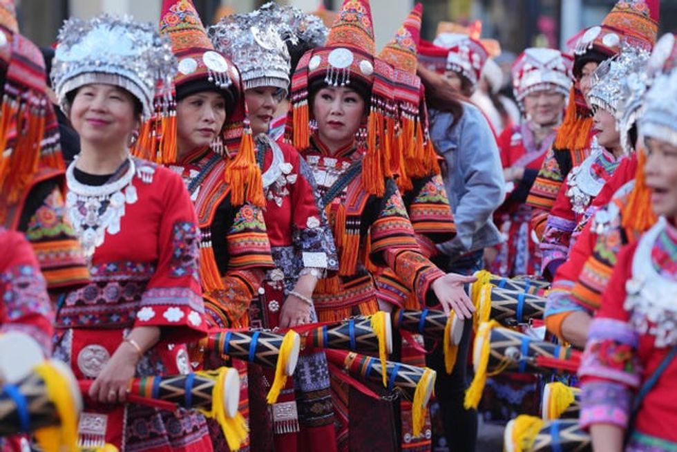 A number of performers in multi-coloured dresses line up