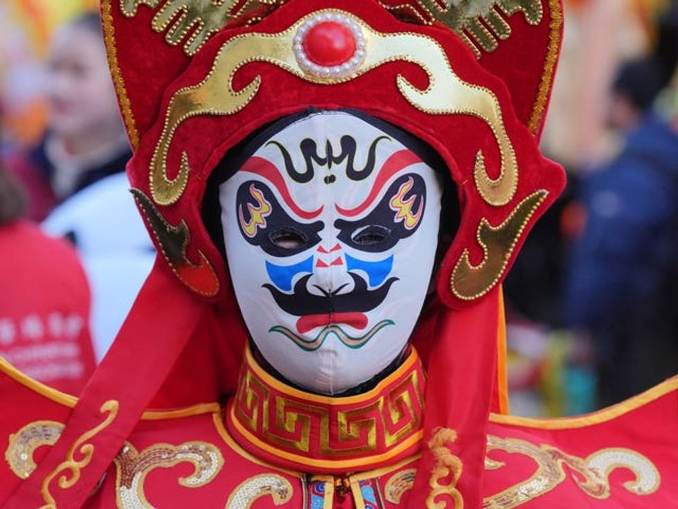 A performer wears a white mask with a design in black, blue, pink and red