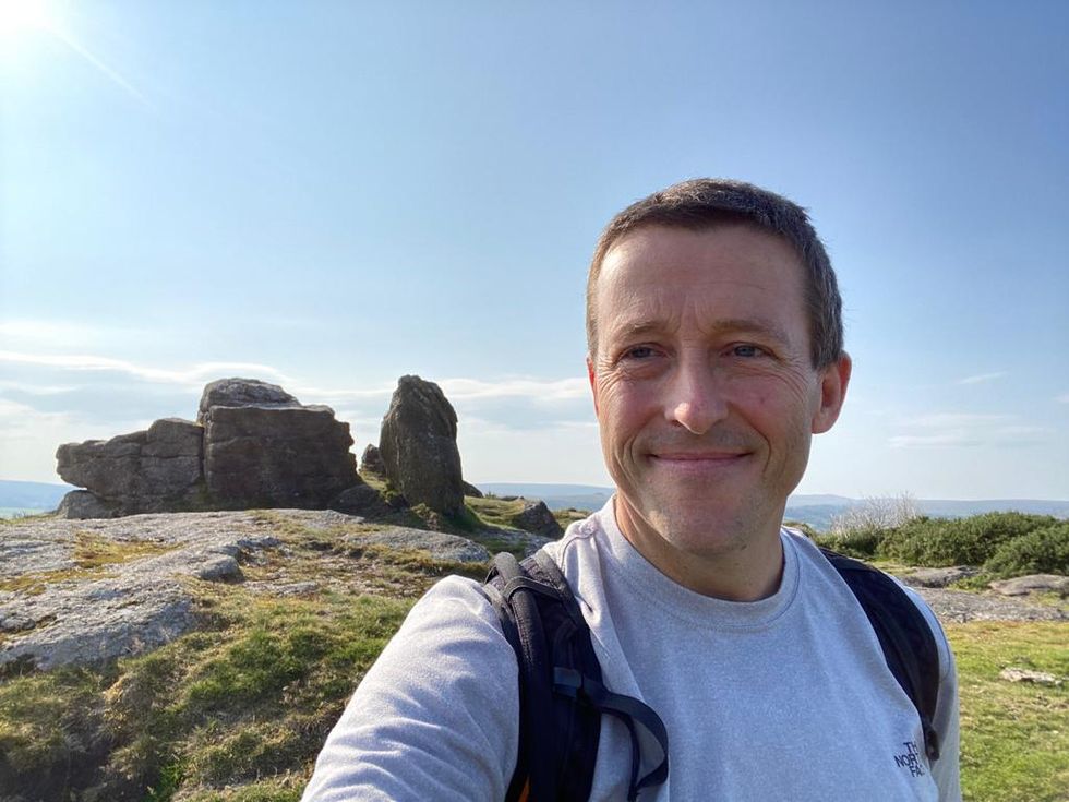A photo of Griff Barnes smiling at the camera with a mountain range behind him