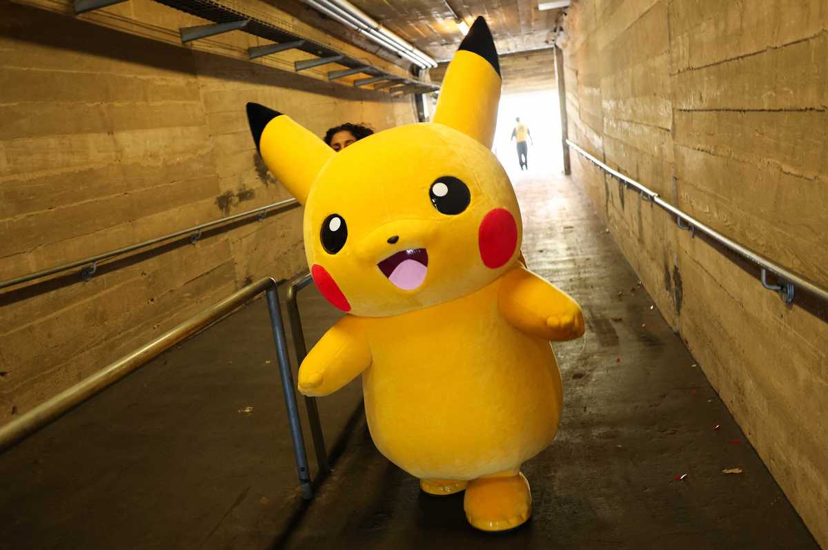 A Pikachu character walks through a tunnel after posing for pictures with fans as people play the Pokemon GO game on smartphones during the in-person Pokemon GO Tour Kalos Los Angeles 2026