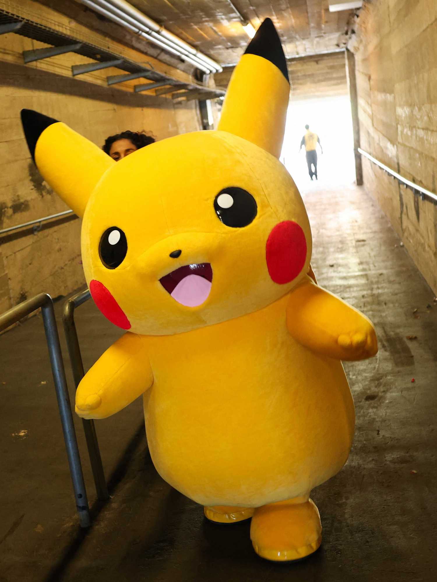 A Pikachu character walks through a tunnel after posing for pictures with fans as people play the Pokemon GO game on smartphones during the in-person Pokemon GO Tour Kalos Los Angeles 2026
