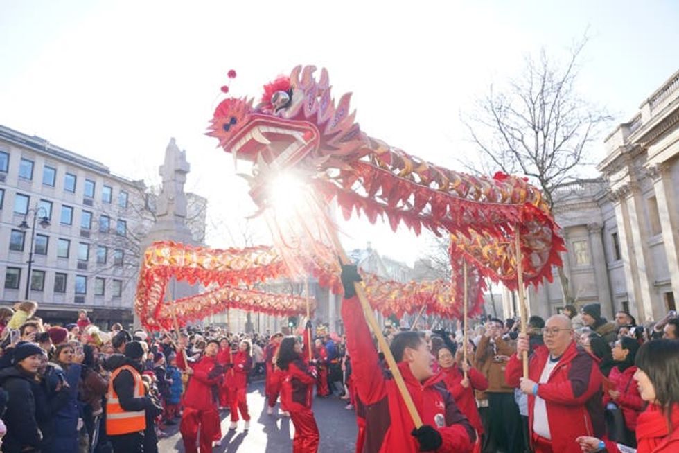 A red dragon model is held in the air by a parade performer