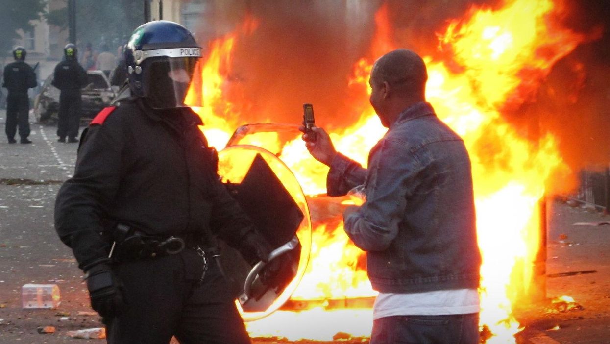 A resident films a police officer on his mobile phone during disturbances in Hackney, London on August 8, 201