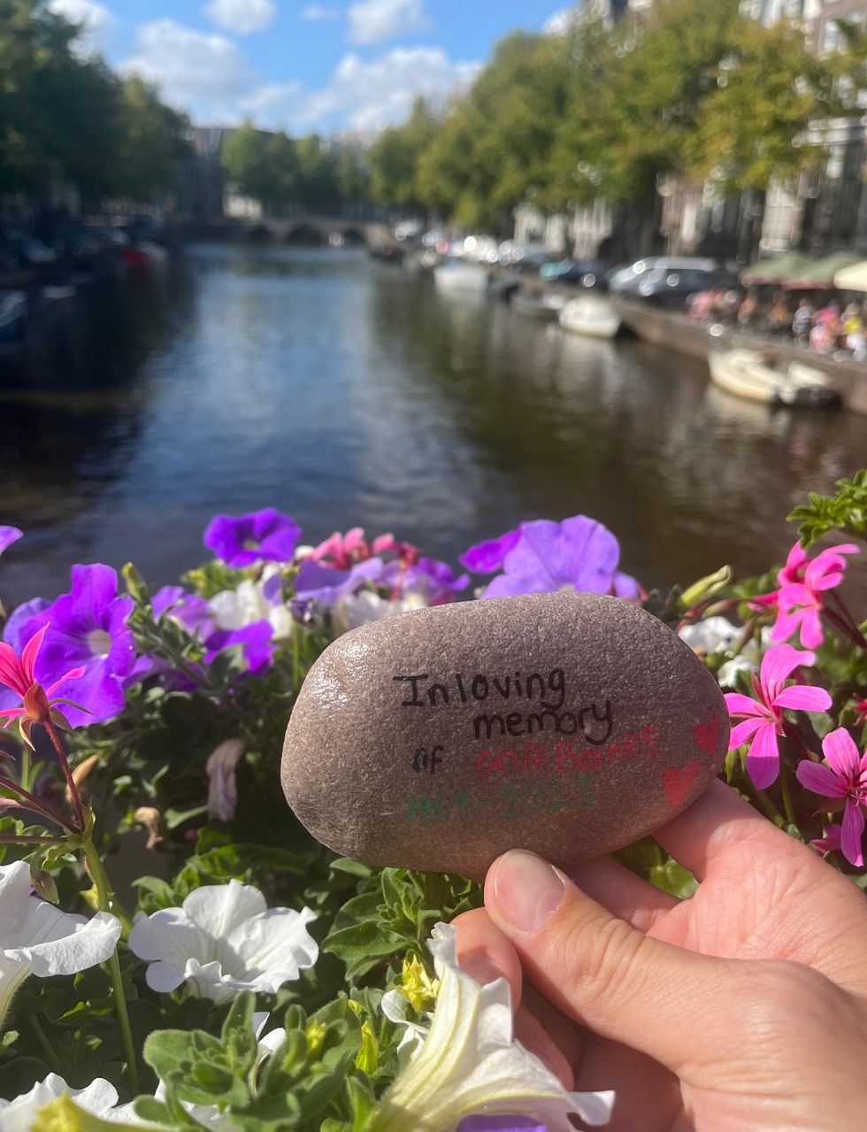 A rock reading the words 'In loving memory of Griff Barnes' held in front of some flowers over a canal in Amsterdam