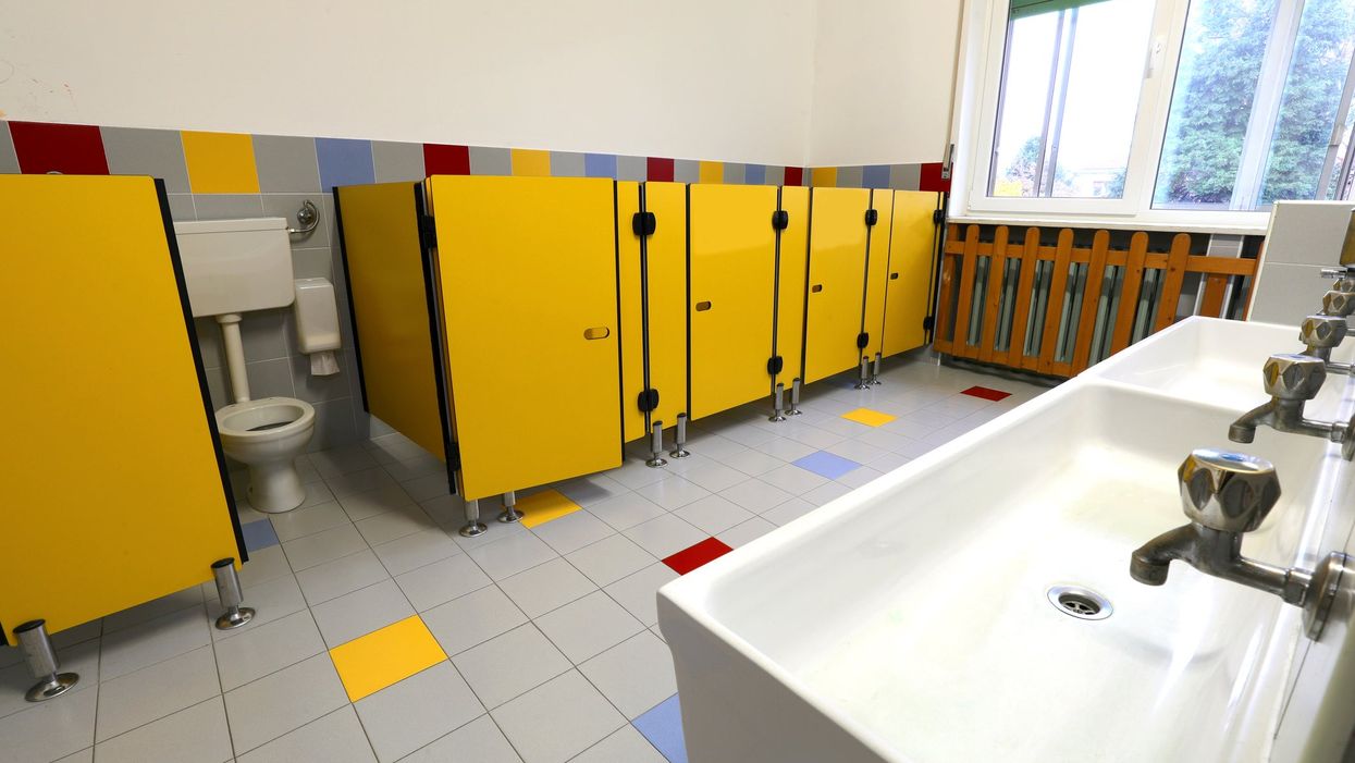 A row of school toilet cubicles with yellow doors. One of them is ajar, showing the toilet inside.