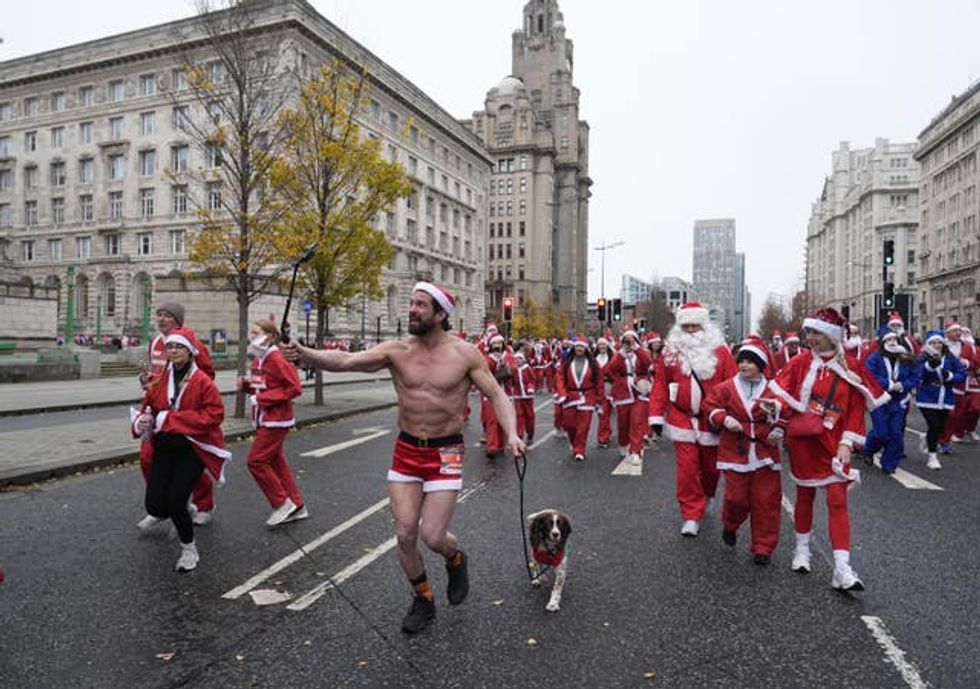 A shirtless Santa runs with a dog in front of a crowd