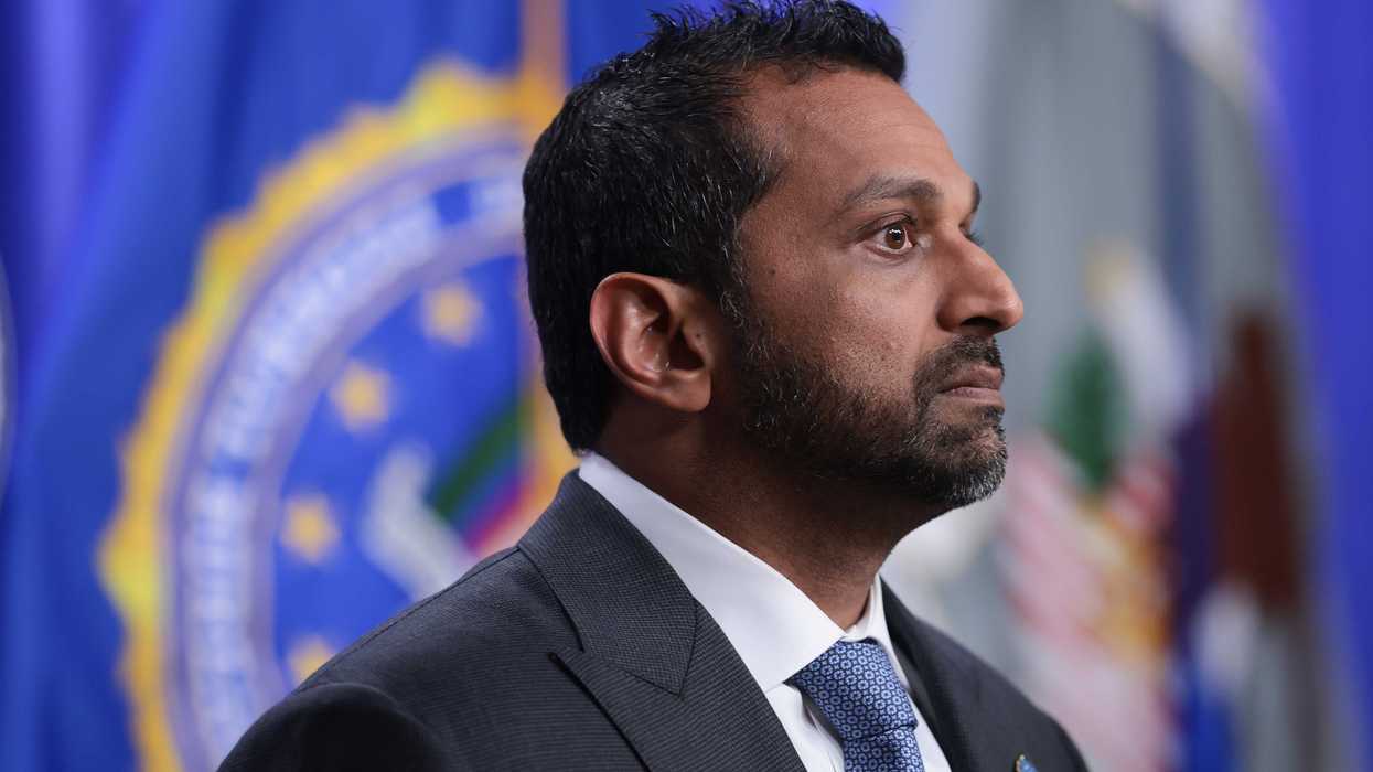 A side-on photo of Kash Patel, a bearded brown man with short black hair and a black suit.