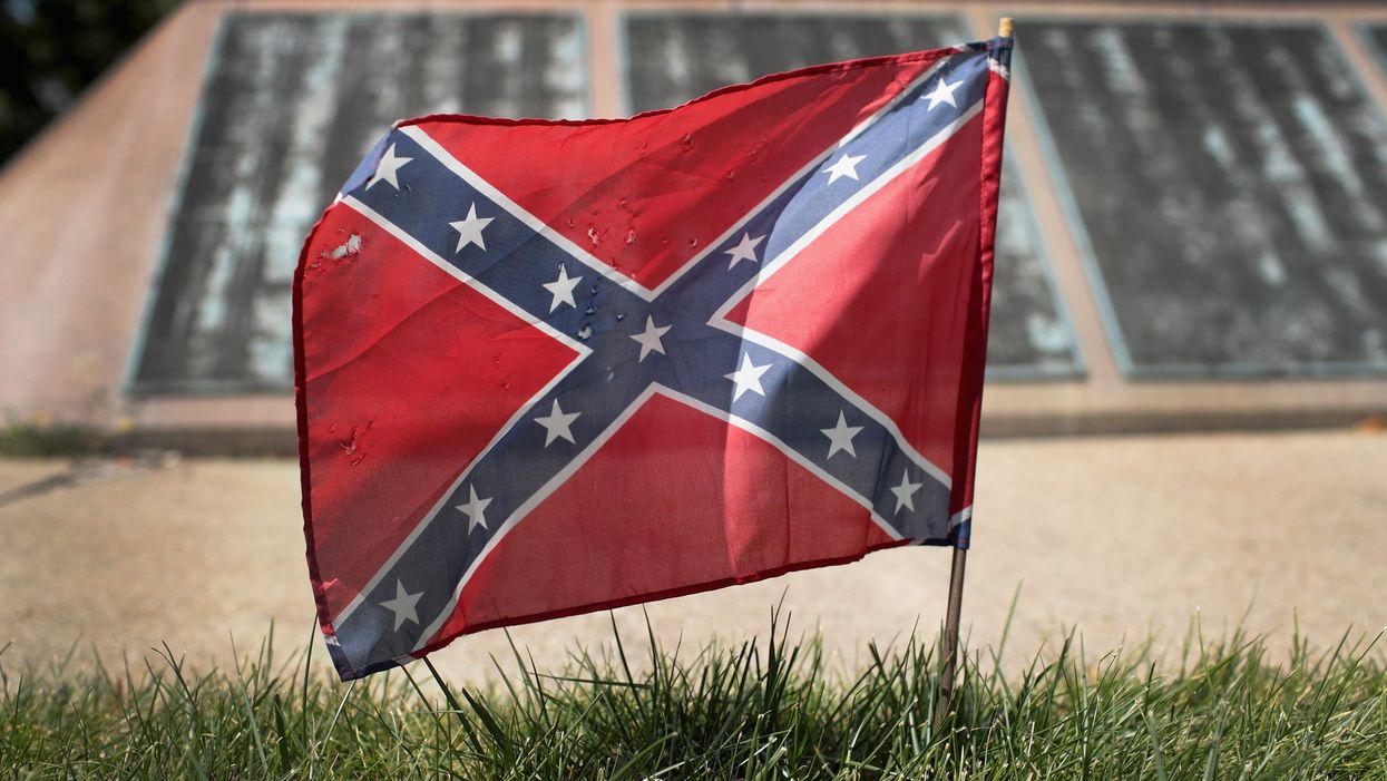 A small Confederate Flag has been placed in the grass in front of what appears to be a memorial.