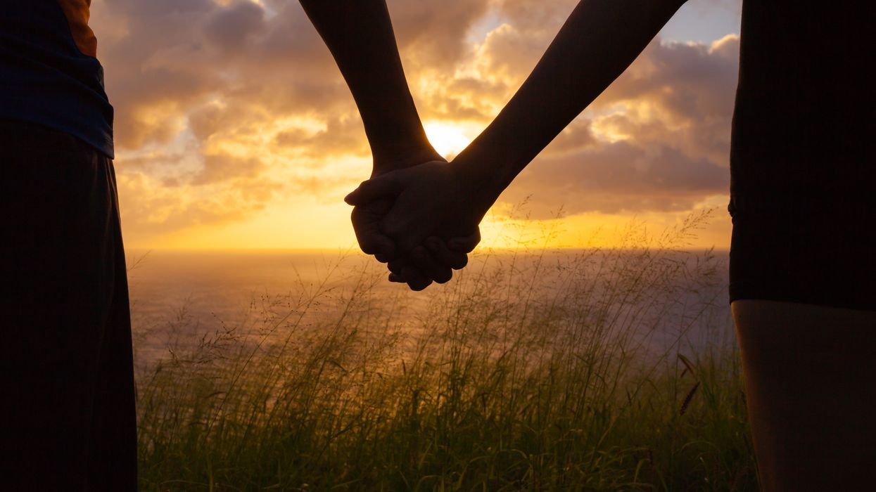 A stock image of a couple holding hands at sunset