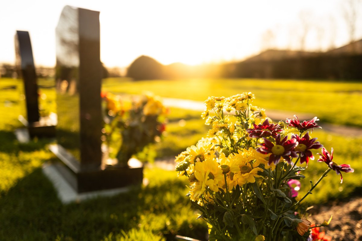 A stock image of dusk at a winter's English cemetery seen with in-focus flowers in a burial plot
