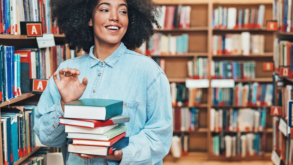 <p>A student holds a stack of books in the library.</p>