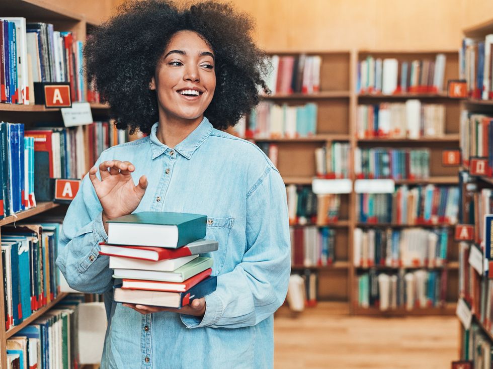 <p>A student holds a stack of books in the library.</p>