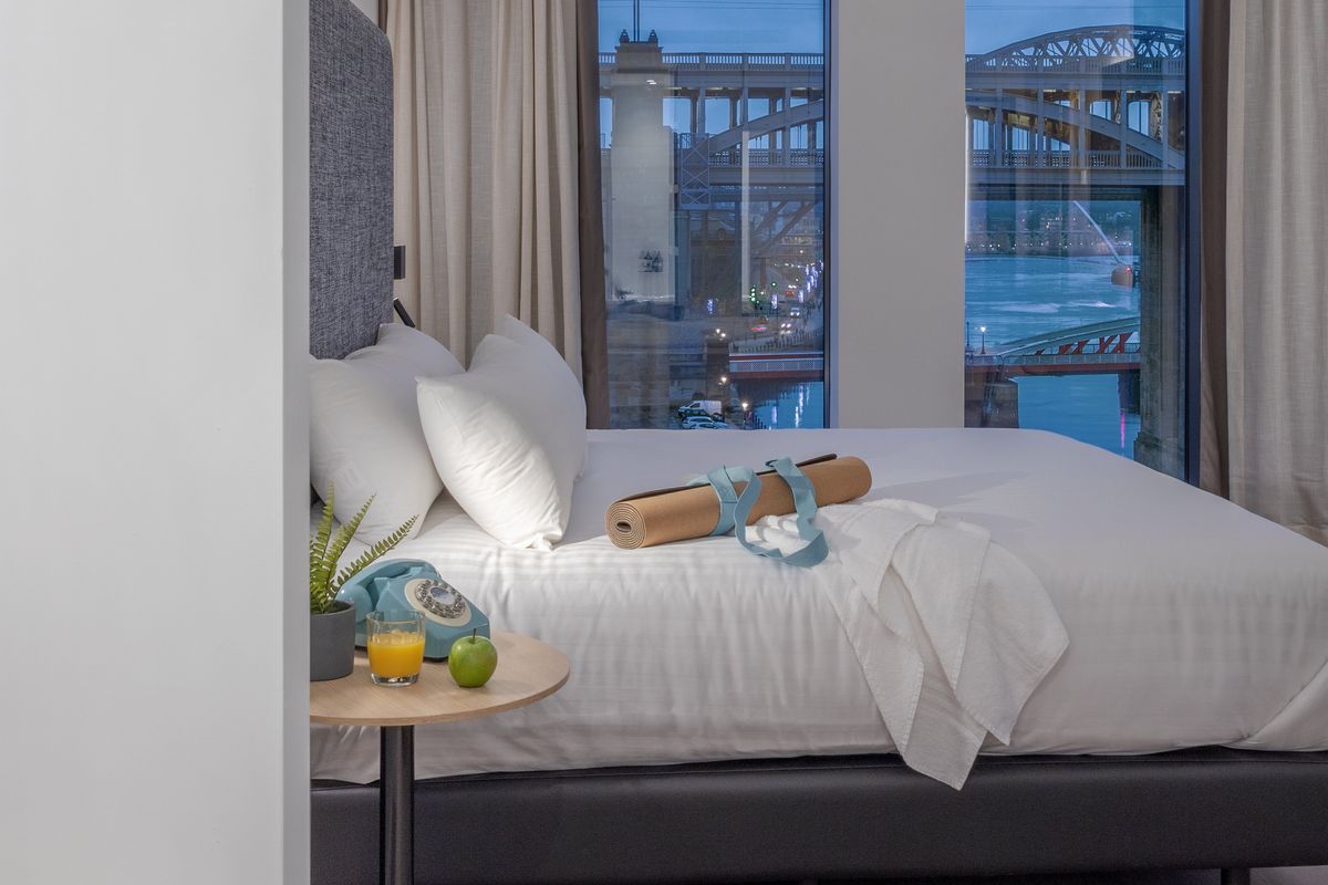 A view of a bedroom at INNSiDE Newcastle, with a yoga mat on the bed. The view from the window is of a bridge