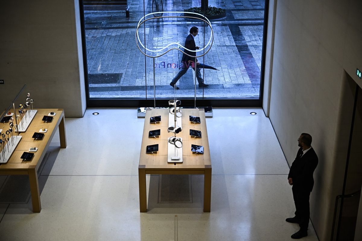 A view over an Apple store layout. The Vision Pro is on display alongside a number of iPads. A security guard watches on.