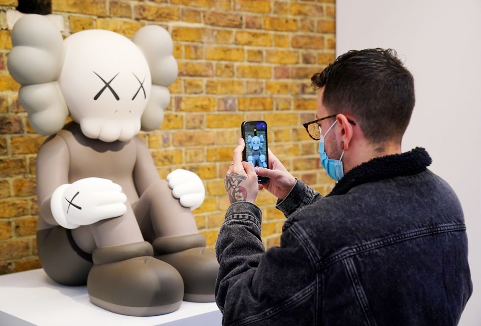 A visitor photographs artwork by Kaws (Jonathan Brady/PA)