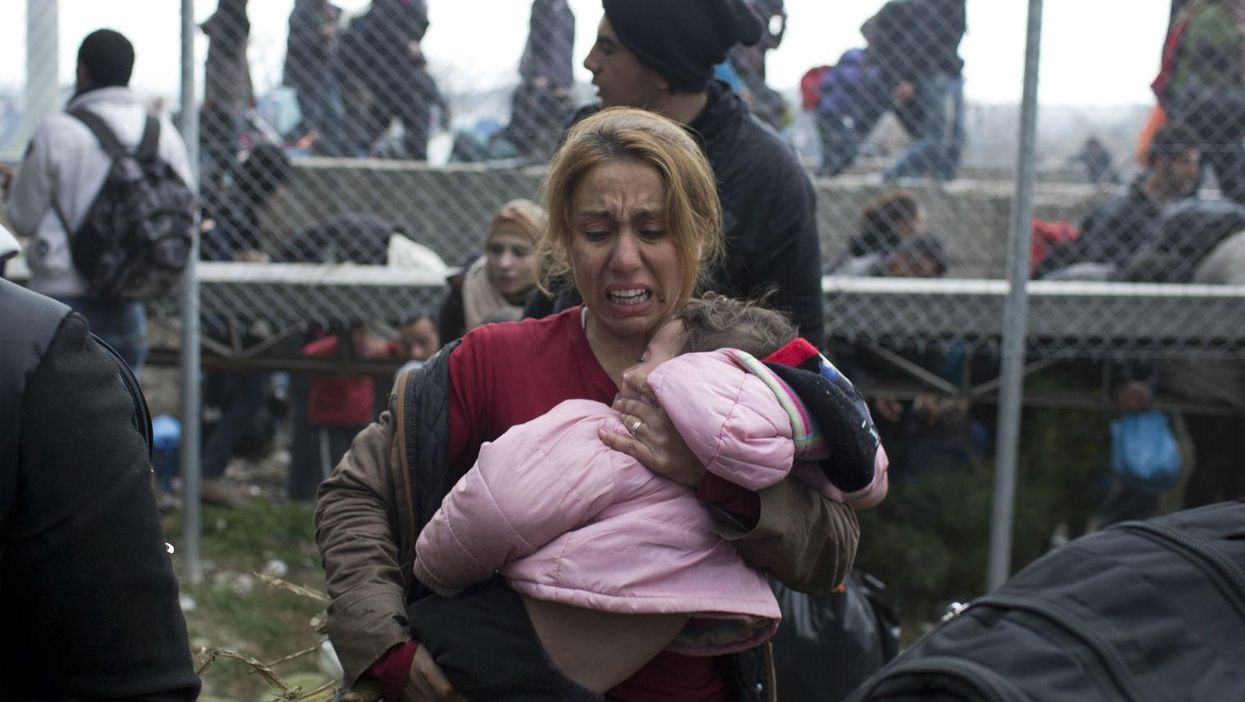 A woman holds her child as she runs away from police firing tear gas on the Greek-Macedonian border, 29th Febraury 2016. Picture: Petros Giannakouris/AP