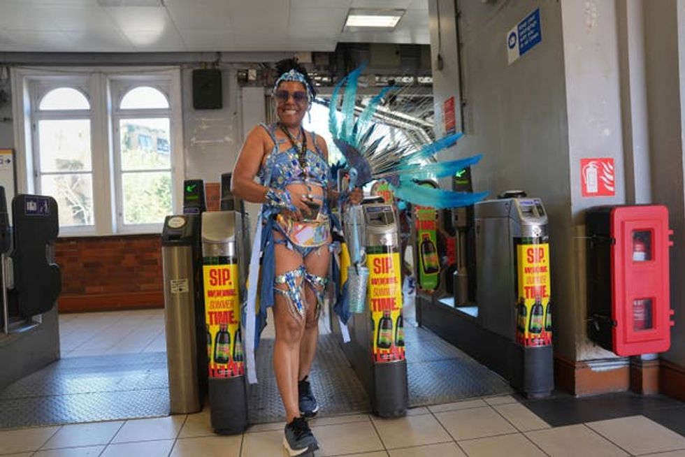 A woman in a blue costume walks through the gates at a Tube station ahead of the Notting Hill Carnival 2025
