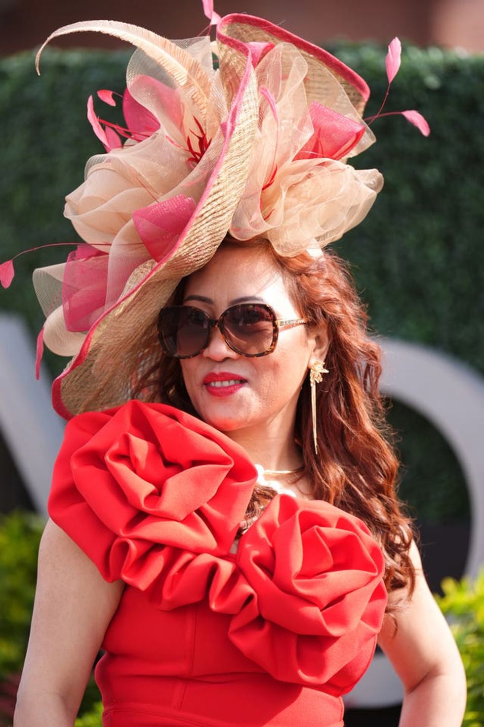 A woman in a large cream and pink hat and a red dress with rose detail
