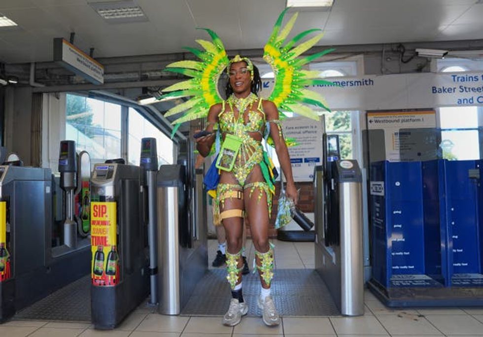 A woman in a yellow and green costume walks through the gates at a Tube station ahead of the Notting Hill Carnival 2025