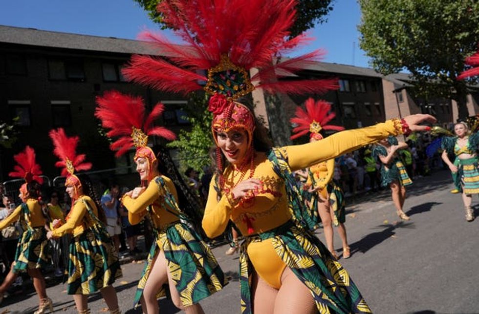 A woman in a yellow leotard with a red feathered headdress smiles at the camera
