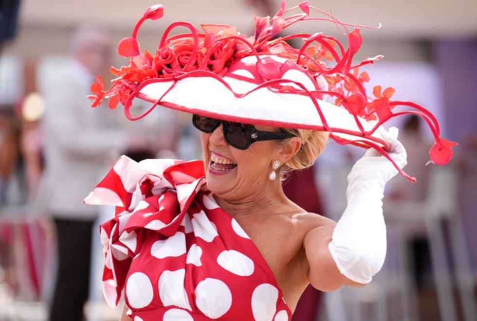 A woman laughing in a red spotty dress and red and white wide-brimmed hat